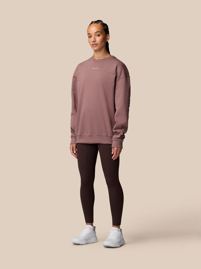 Female model wearing mauve ADAPT LIFESTYLE SWEATSHIRT with oversized fit and crew neckline, paired with dark leggings