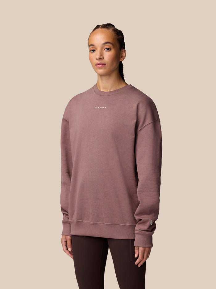 Model wearing mauve oversized sweatshirt with small white Castore logo on the chest
