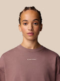 Portrait of a model wearing a mauve crewneck sweatshirt with a small Castore logo on the chest