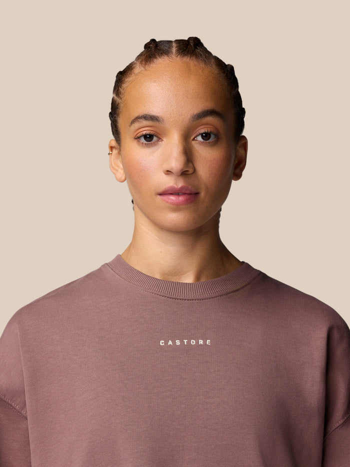 Portrait of a model wearing a mauve crewneck sweatshirt with a small Castore logo on the chest