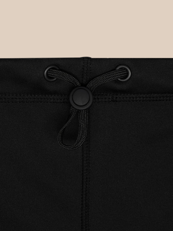 Top edge close-up of black snood showing drawstring with a round stopper and grommets