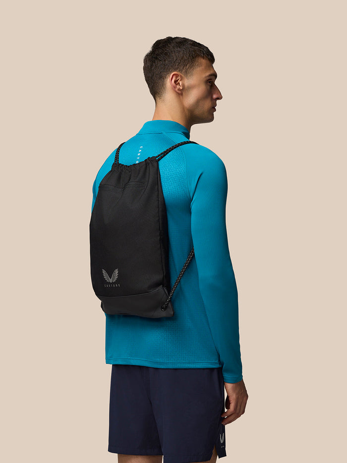 Unisex black gym sack worn as a backpack by a man in a teal top; two straps and a Castore logo at the bottom.