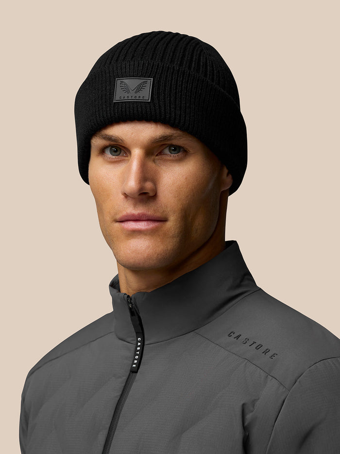 Male model wearing black ribbed Castore beanie and gray jacket