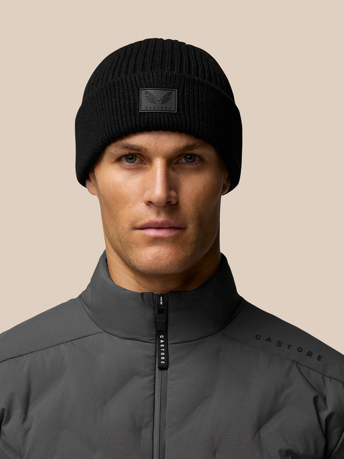 Close-up of a model wearing a black ribbed Castore beanie with front logo patch.