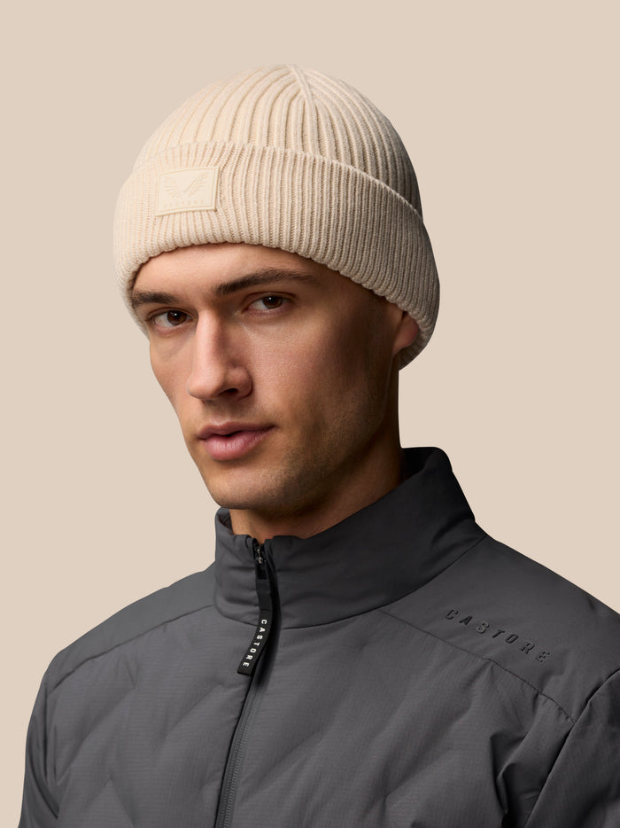 Stone ribbed knit beanie on a model with Castore logo patch at the foldover