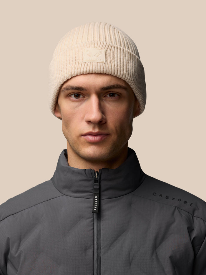 Beige ribbed knit beanie with Castore logo patch on folded brim worn by a model