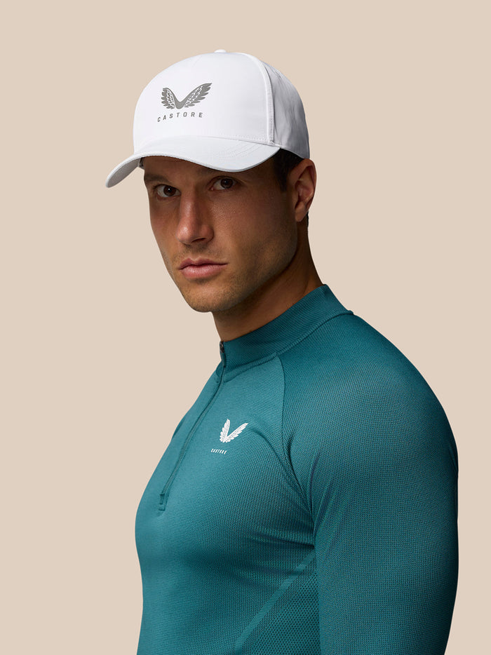 White Castore Core Cap with halo eyelets and adjustable back strap worn by a model in teal athletic top.