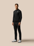 Male model wearing black Club Golf Trousers with matching top and white golf shoes against a beige background