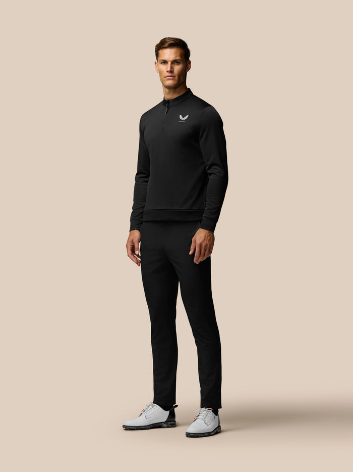 Full body shot of a male model in a black long sleeve zip neck top with a small logo on the chest