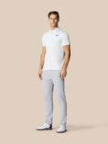Male model in white polo and light grey golf trousers standing against a beige backdrop