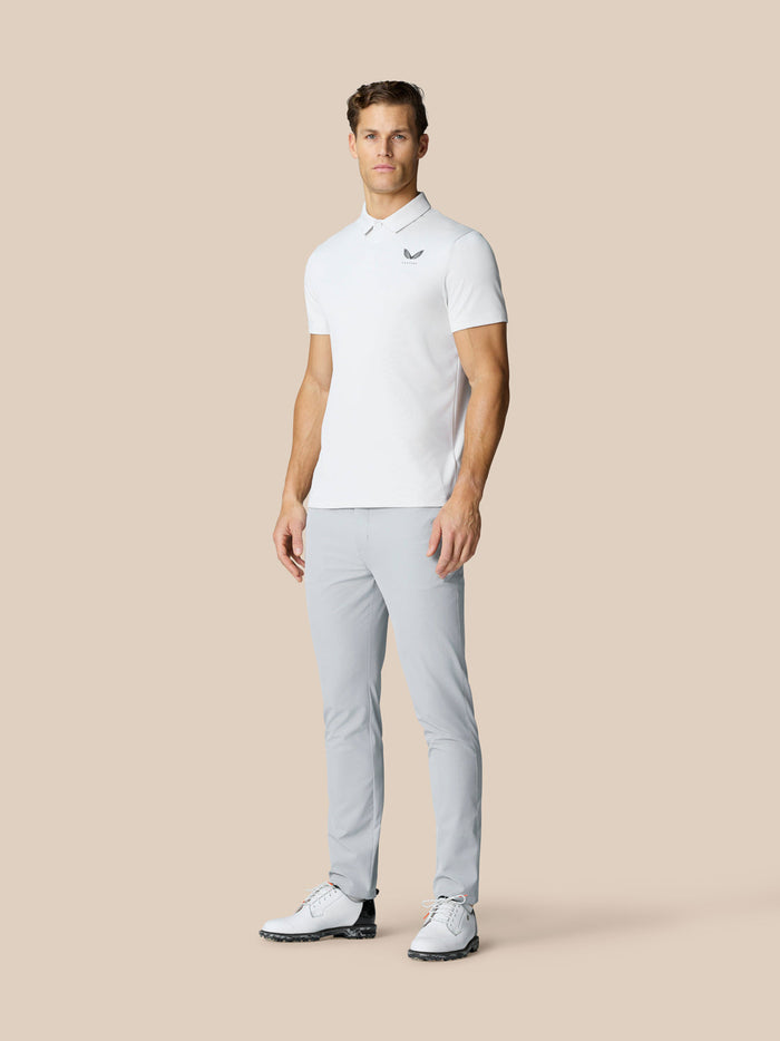 Male model in white polo and light grey golf trousers standing against a beige backdrop