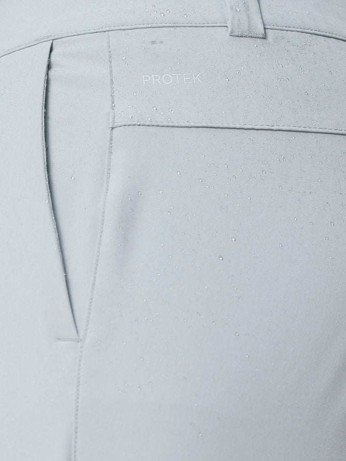 Close-up of light grey golf trousers showing ProTek branding on the back pocket with water droplets.