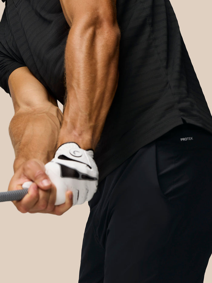 Close up of a golfer gripping a club in a black Pinnacle Pique Stripe polo with subtle stripes