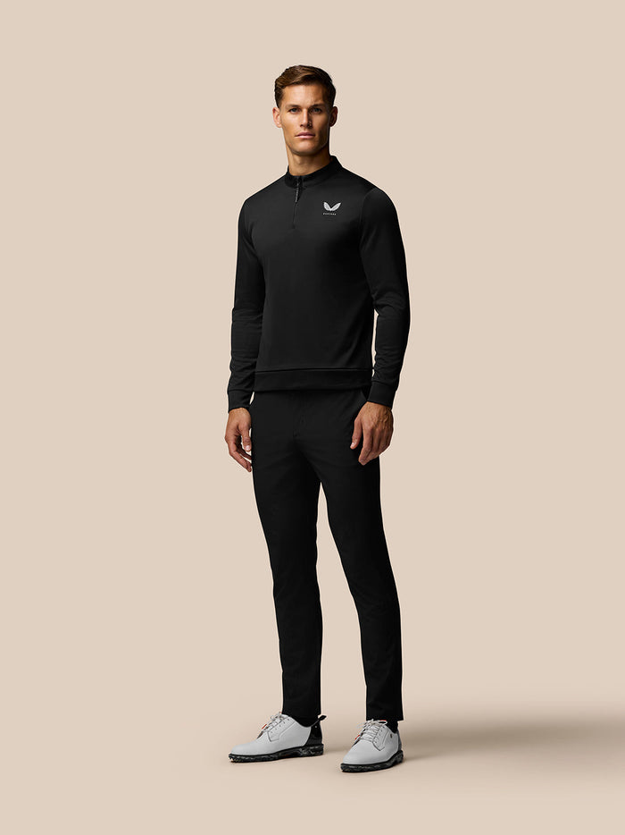 Male model wearing black Golf Club Classic 1/4 zip top with stand collar on a beige background
