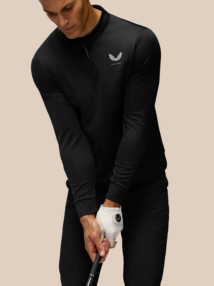 Man wearing black Golf Club Classic 1/4 zip top gripping a golf club with a left chest logo visible
