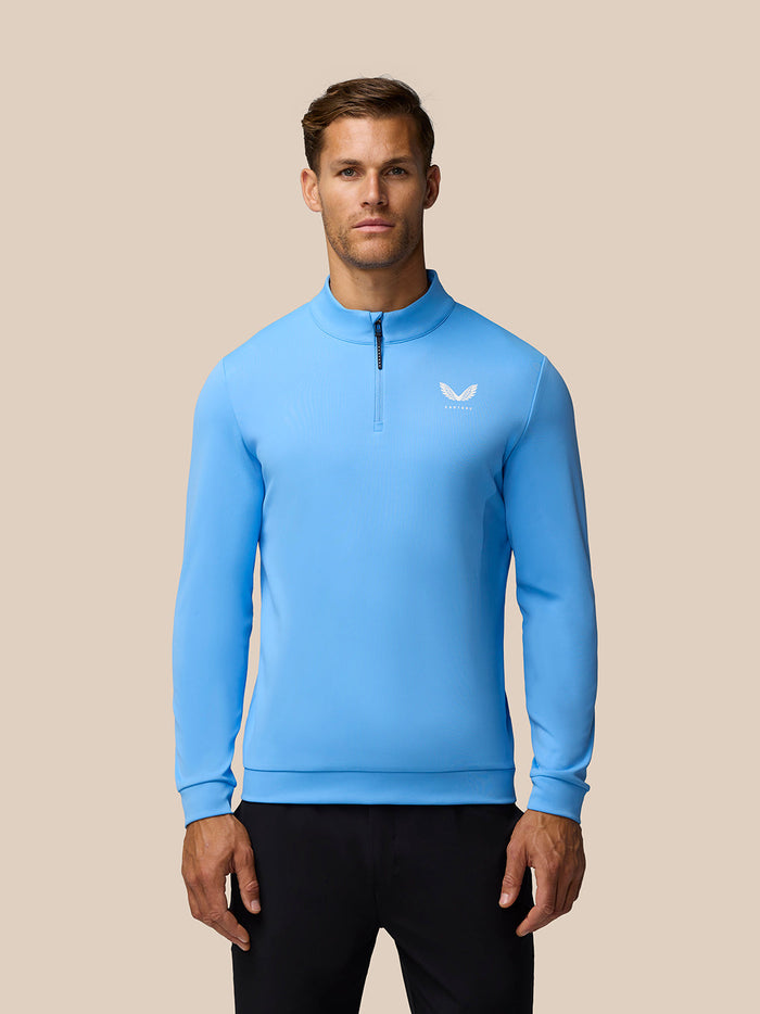 Front view of man wearing light blue Golf Club Classic quarter zip top with funnel collar and Castore logo on left chest
