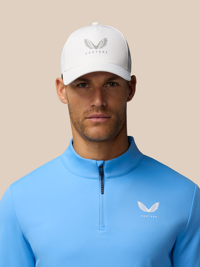 Close-up of a man wearing a white Castore cap and cool blue Golf Club Classic 1/4 Zip Top with funnel collar