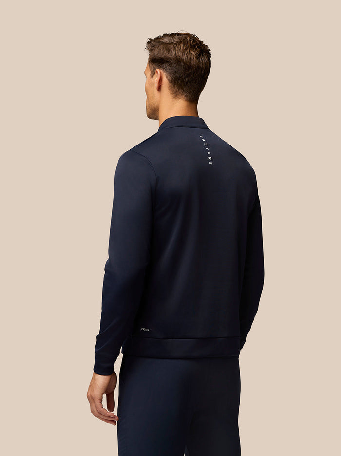 Back view of midnight navy golf top showing a vertical Castore logo on the upper back and Protek branding at the lower back.