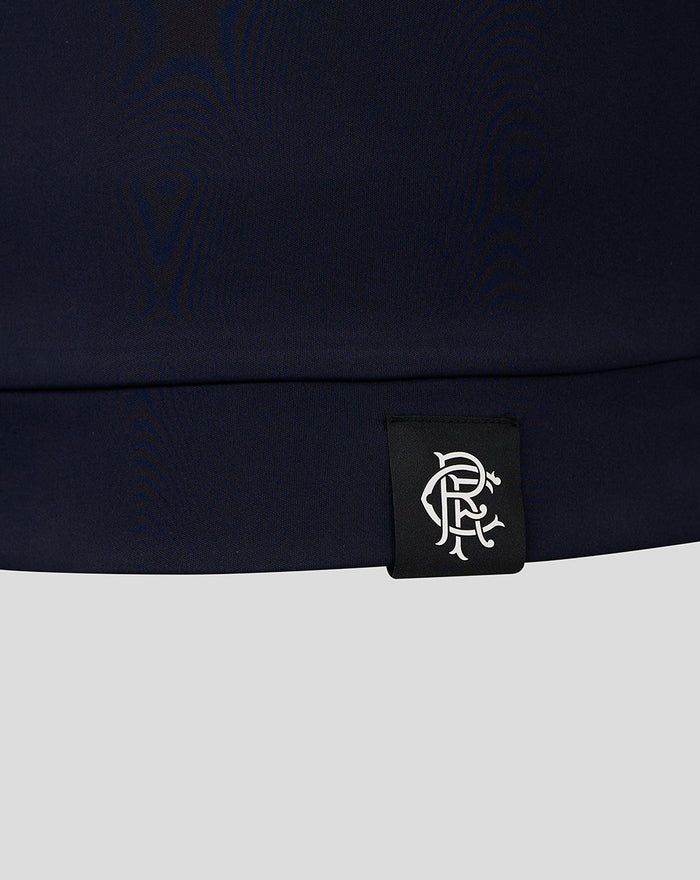 Close-up of navy fabric hem with black tag bearing a white Castore crest logo.