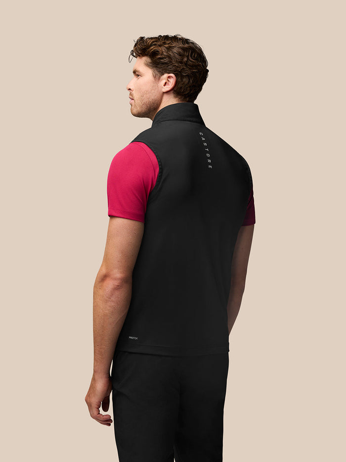 Back view of a man wearing a black Pinnacle Gilet over a pink polo; Castore branding along collar and zipper.