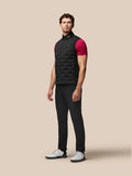 Full-body shot of a male model in a black Pinnacle Gilet with quilted panels over a dark outfit and white sneakers.