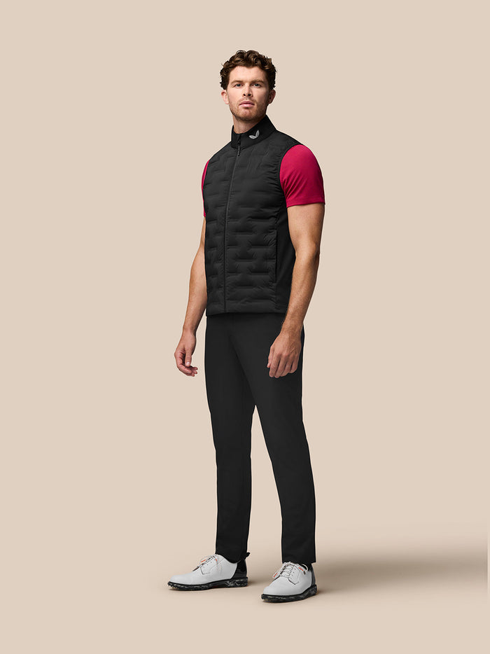Full-body shot of a male model in a black Pinnacle Gilet with quilted panels over a dark outfit and white sneakers.