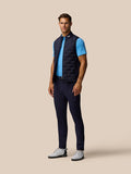 Full-body view of a man in a navy Pinnacle gilet over a light blue polo, front zipper and stand collar visible.