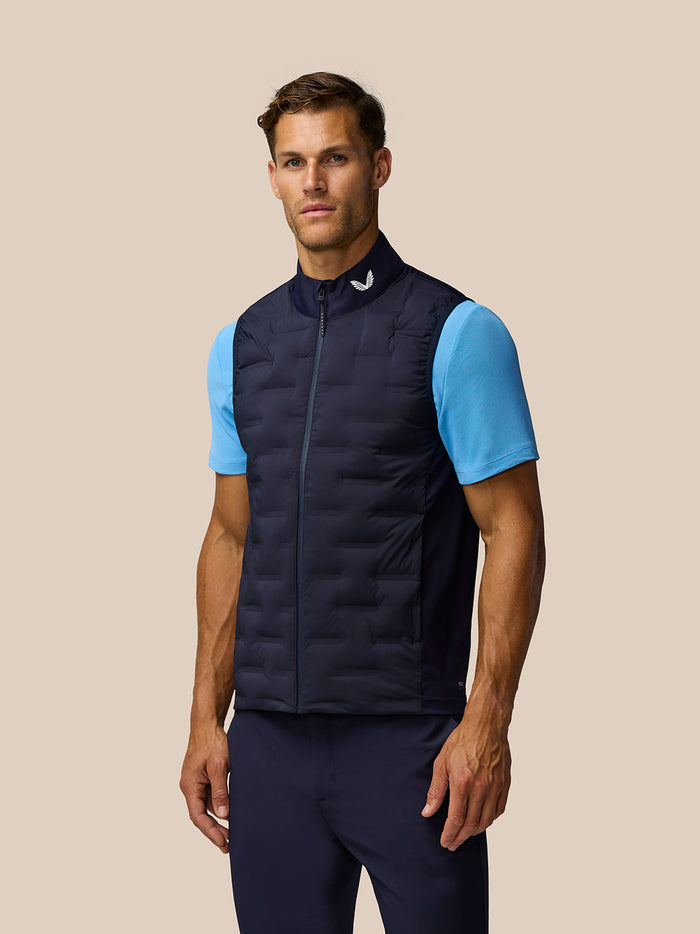 Male model wearing navy Pinnacle gilet with light blue sleeves against a beige backdrop