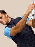 Side-angle of golfer wearing navy Pinnacle Gilet with blue underlayer mid swing, Castore logo on collar