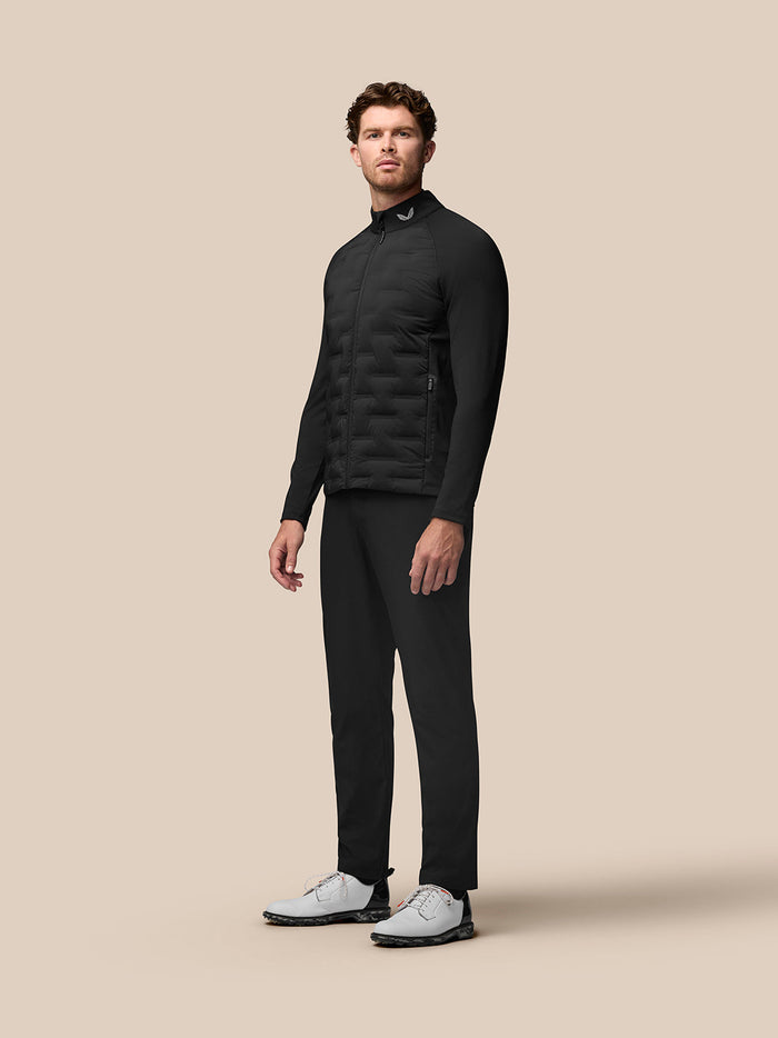 Male model wearing black Castore Golf Pinnacle Jacket with stand collar and quilted front panels.