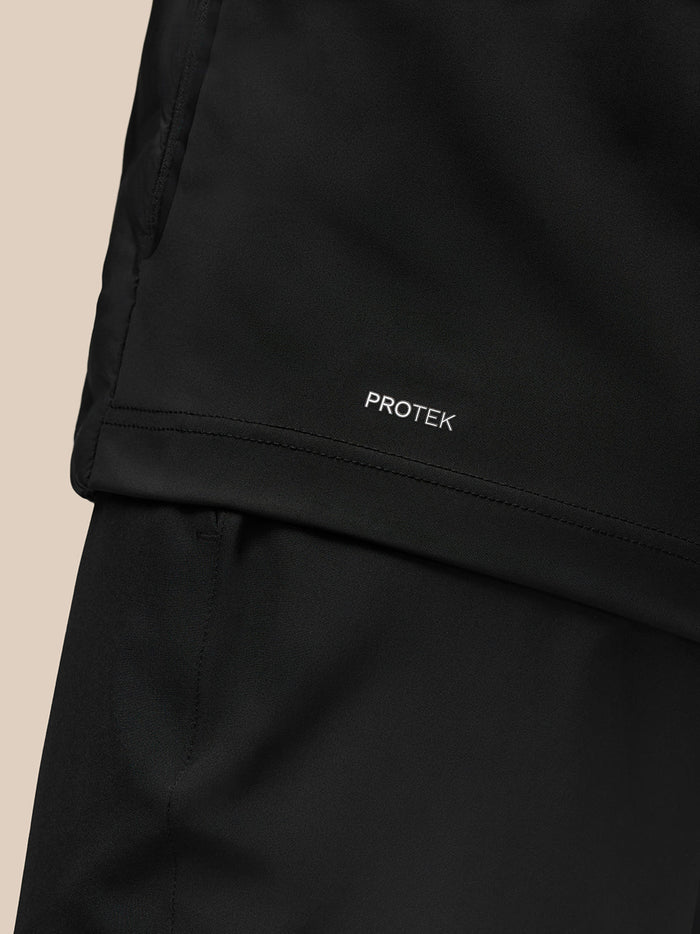 Close-up of lower back of black Pinnacle Golf Jacket showing PROTEK branding at the hem