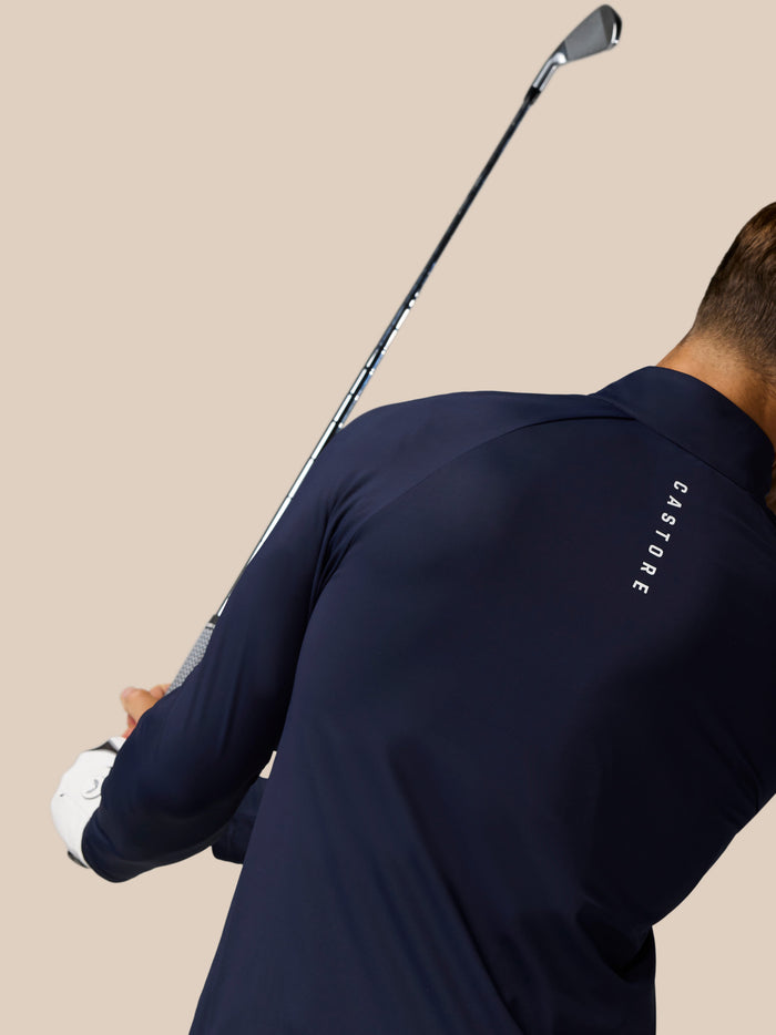 Back view of navy golf pinnacle jacket worn by a golfer with raglan sleeves and stand collar
