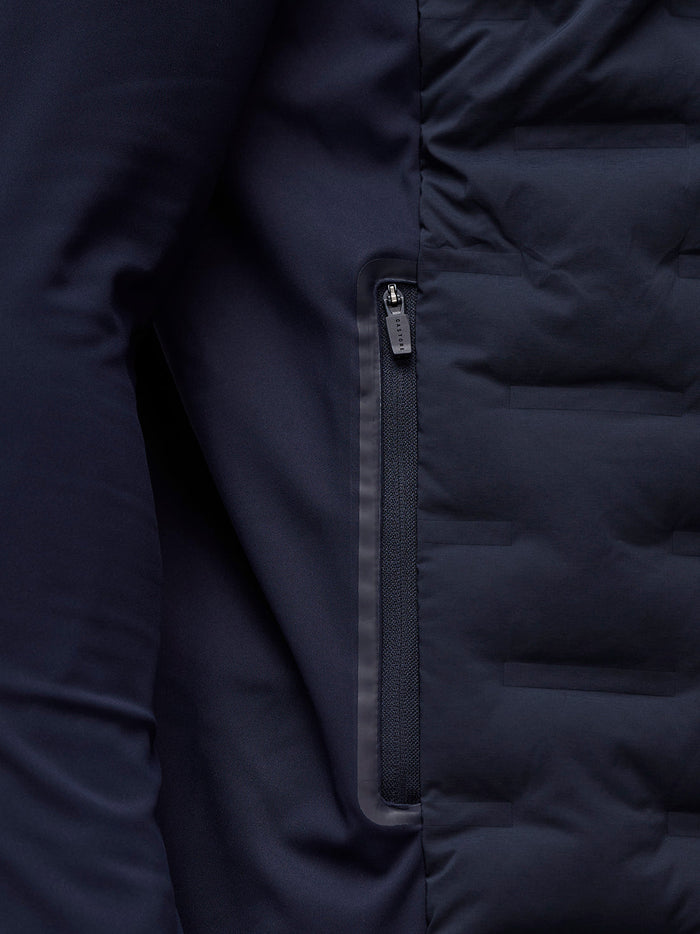 Close-up of navy Castore golf pinnacle jacket showing a zippered chest pocket and quilted front panels