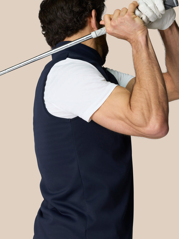 Side view of man wearing navy Club 1/2 Zip Gilet with high neck and sleeveless design, holding a golf club.