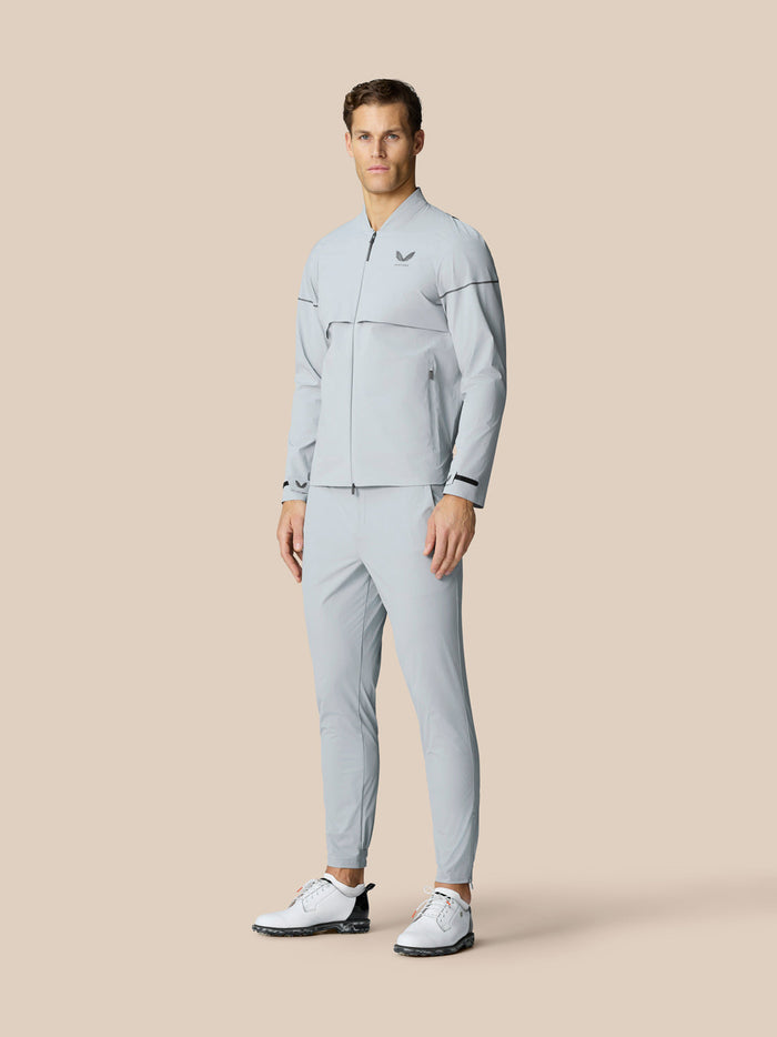 Full body shot of a male model in a light grey LVS woven golf jacket with matching pants and white golf shoes.
