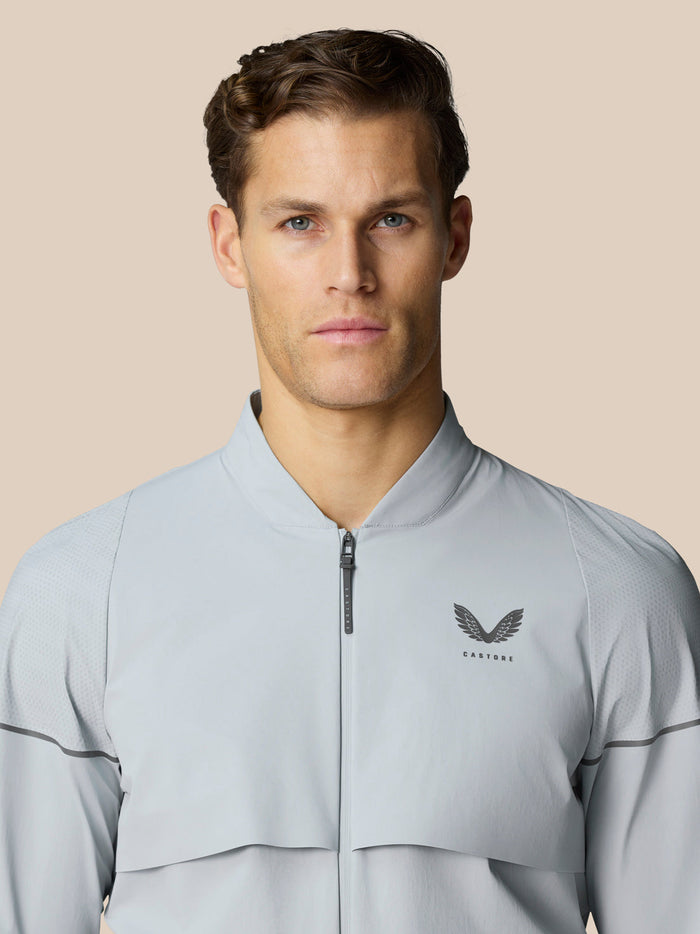Male model wearing light grey Castore golf pinnacle LVS woven jacket with zip against a neutral background.