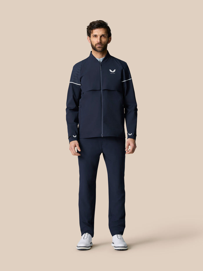 Full body shot of a man wearing the midnight navy Golf Pinnacle LVS Woven Jacket with zip front and white sleeve piping.
