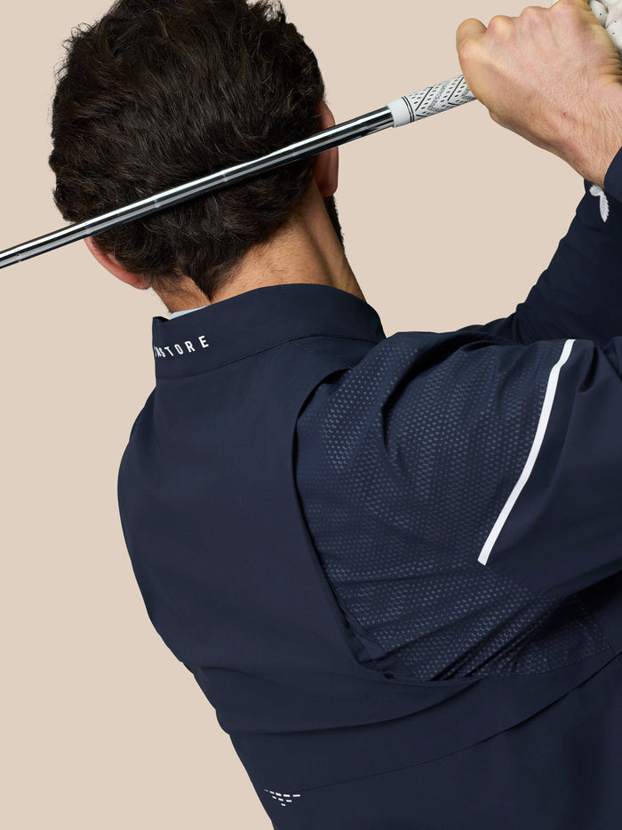 Rear view of golfer wearing midnight navy LVS woven jacket during a swing