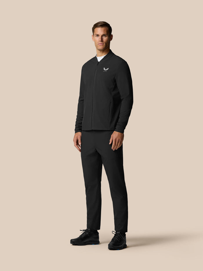 Male model wearing black golf winter trousers and matching jacket standing against a beige background.
