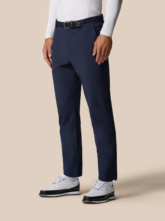 Male model wearing midnight navy golf winterised trousers with woven belt and white sneakers