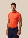 Male model wearing bright orange Pinnacle Golf polo with striped knit and Castore logo on left chest