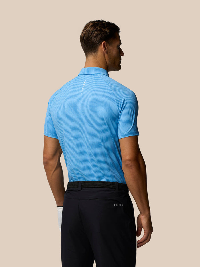 Back view of a man wearing a light blue Glow Printed Polo with subtle pattern and small logo at upper back.