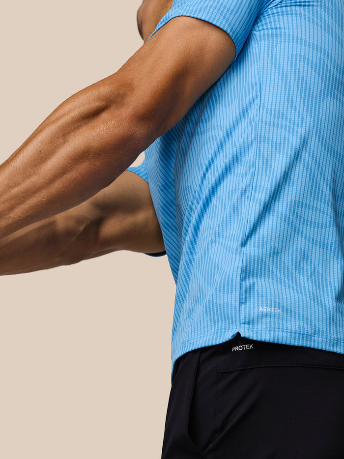 Male golfer wearing blue Glow Printed Polo with AerTek fabric and a side split hem
