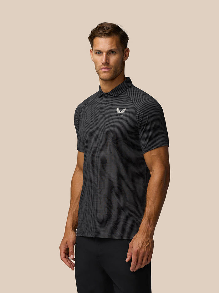 Front view of a man wearing gunmetal gray glow printed polo with allover pattern and Castore logo on the left chest