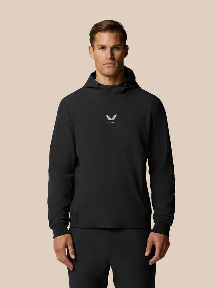 Front three quarter view of a man in a black Castore Golf Pinnacle Performance Hoodie with a center chest logo.