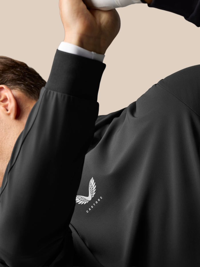 Close-up of a golfer in the black Golf Pinnacle Performance Hoodie with a chest Castore logo and a raised arm