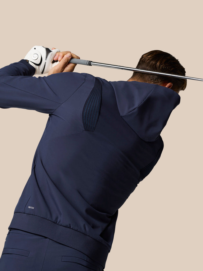 Back view of golfer in midnight navy Castore hoodie mid swing with ProTek badge.