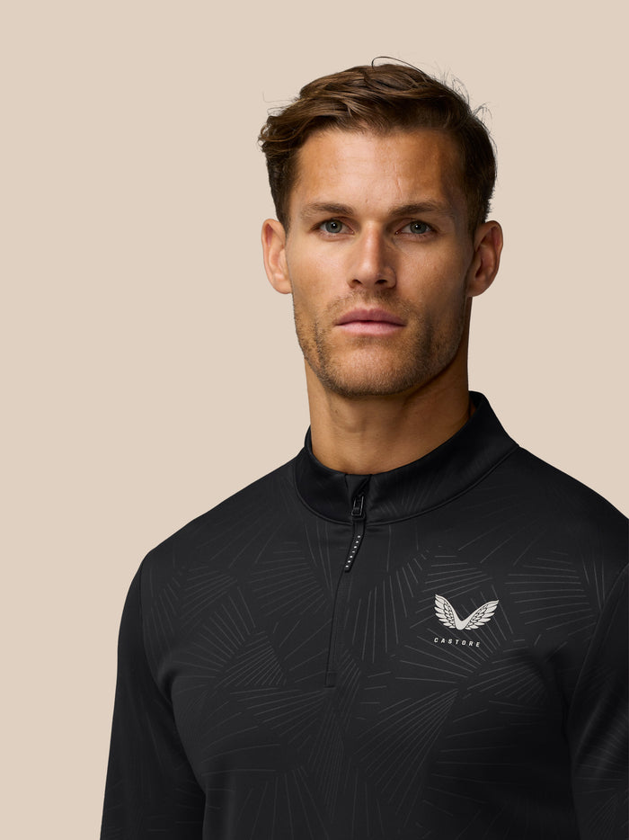 Close-up of male golfer wearing black Golf Club Classic quarter-zip top with all-over print and Castore logo on left chest.