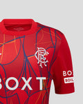 Shoulder and chest of red Rangers FC junior away goalkeeper shirt featuring crest and vibrant abstract pattern.
