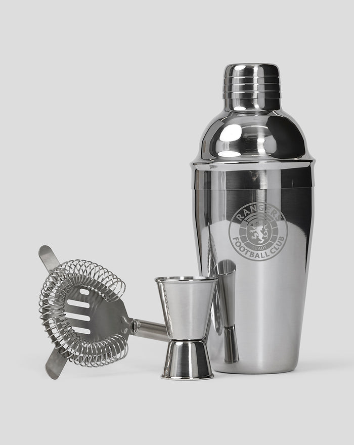 Shiny stainless steel three piece cocktail shaker set with a strainer and jigger on a light gray background